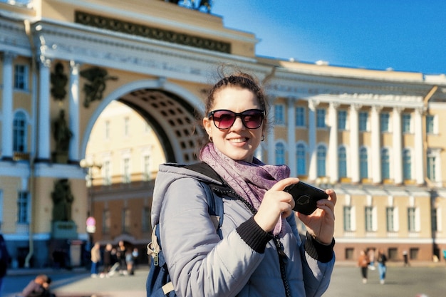 Grão de filme de ruído artístico. Mulher jovem turista de retrato com telefone, levanta e tira fotos de pontos turísticos de São Petersburgo. Conceito de viagens incríveis e aventuras inesquecíveis. Copie o espaço