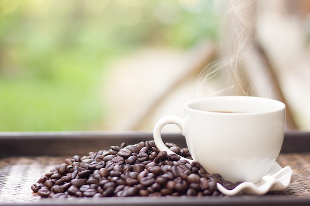 Grãos de café com caneca de café branco desfocagem o fundo, uma xícara de café quente é colocada ao lado dos grãos de café