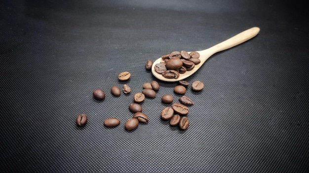 Foto grãos de café com uma colher de bambu em um prato preto