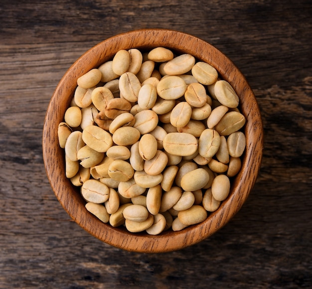 Grãos de café crus em uma tigela de madeira na mesa de madeira