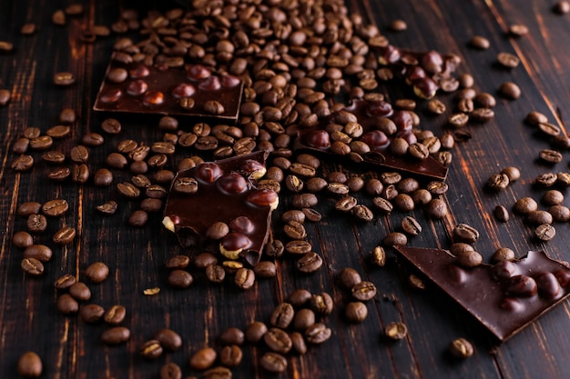 Grãos de café dispersados e chocolate preto em uma tabela de madeira.