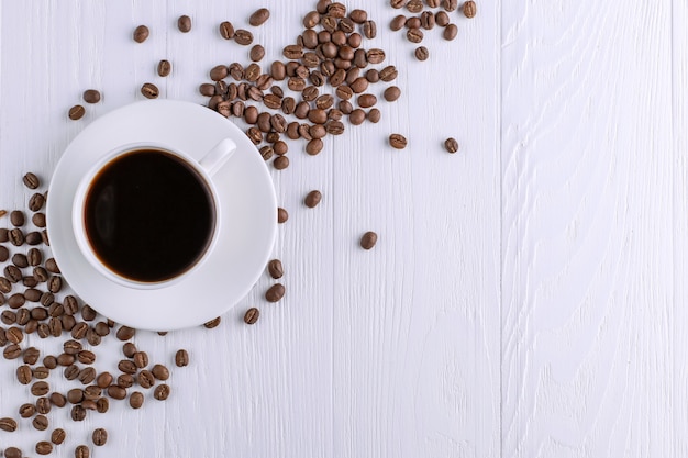 Grãos de café dispersados, um copo e chocolate preto em uma mesa de madeira branca. copie o espaço.