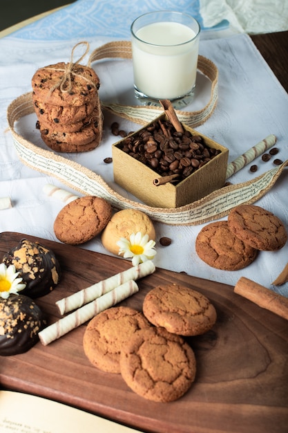 Grãos de café e biscoitos de manteiga com um copo de leite na placa de madeira