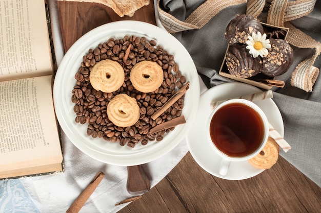 Grãos de café e biscoitos em um pires com uma xícara de chá