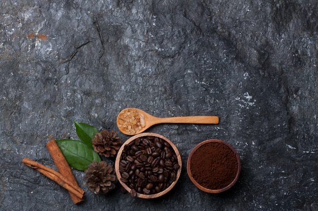 Grãos de café em copo de madeira, açúcar em pinho colher de madeira e folhas em fundo preto de pedra