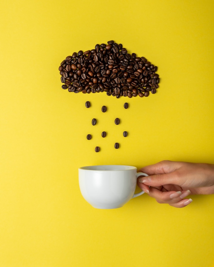 Foto grãos de café em forma de nuvem chuvosa com xícara branca na superfície amarela.