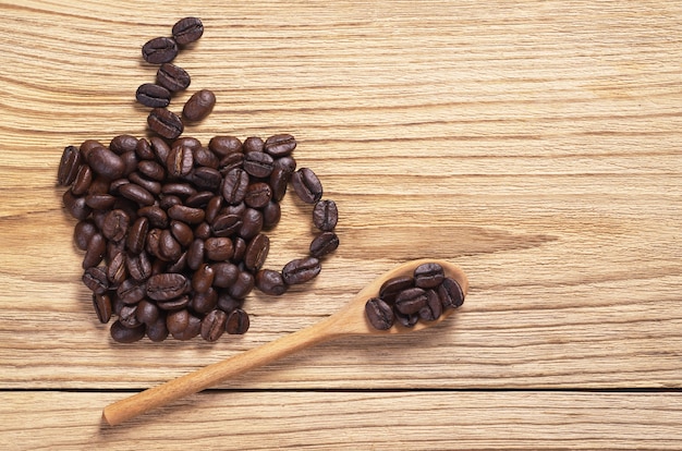 Grãos de café em forma de xícara e colher na mesa de madeira, vista superior