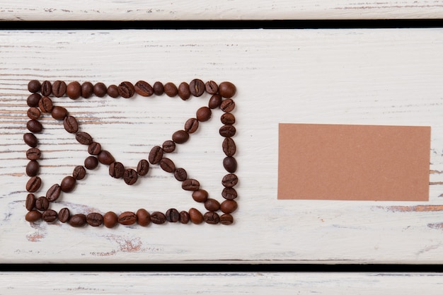 Foto grãos de café em madeira dispostos em um símbolo de envelope. fundo branco da vista superior.