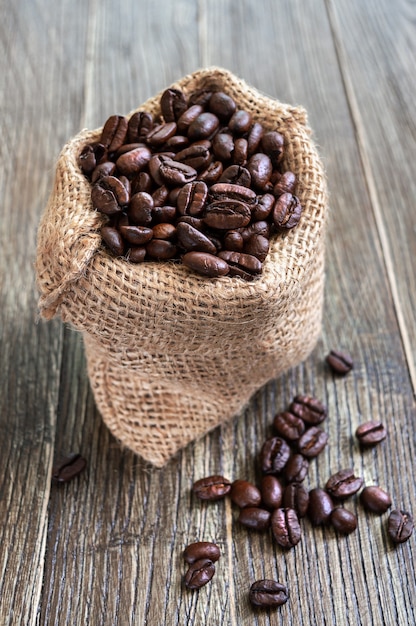 Grãos de café em saco de saco em um fundo de madeira. visão vertical