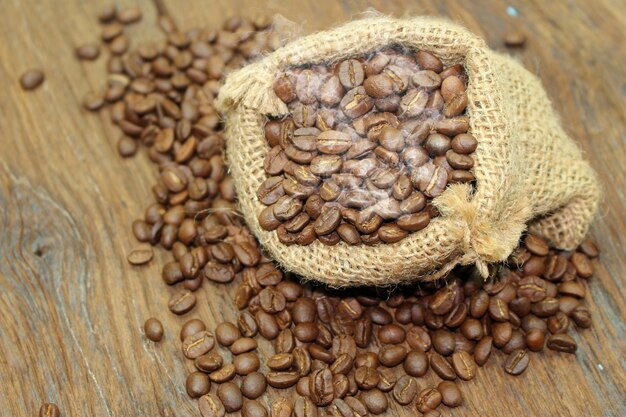 Grãos de café em um saco de saco em fundo de madeira