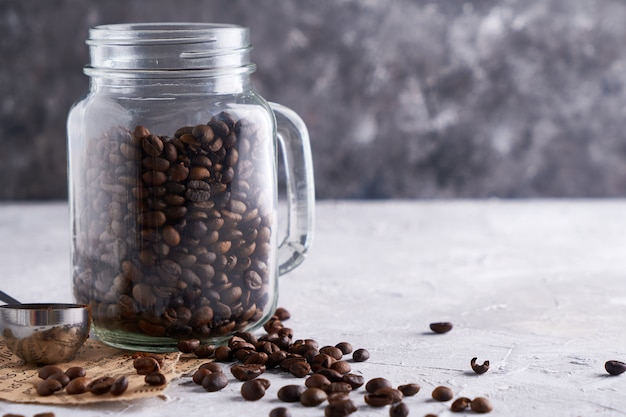 Grãos de café em uma jarra de vidro sobre uma mesa cinza