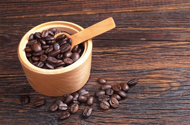 Grãos de café em uma tigela com uma colher na mesa de madeira escura