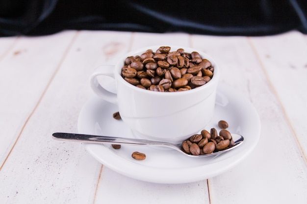 Grãos de café em uma xícara branca em uma mesa de madeira