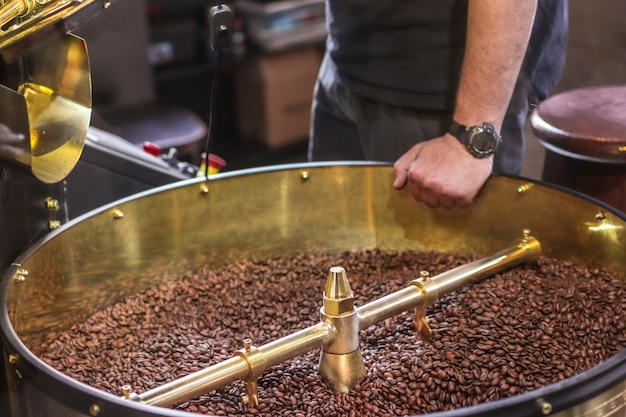 Grãos de café escuros e aromáticos em uma moderna máquina de torrefação