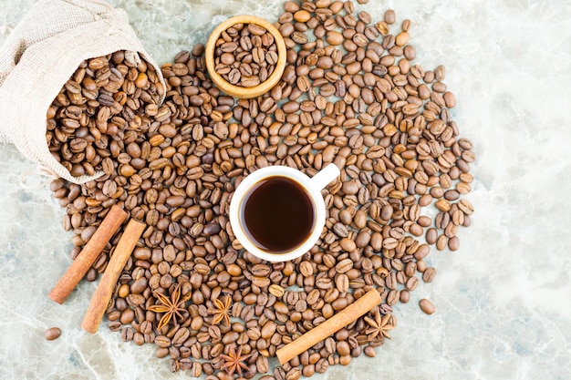 Grãos de café espalhados em uma mesa de mármore com uma xícara de café aromático. Paus de canela e anis estrelado para melhorar o sabor do café. vista do topo.