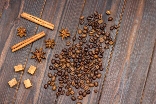 Grãos de café espalhados na mesa, anis estrelado, paus de canela e pedaços de açúcar mascavo.