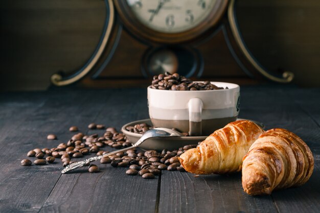 Grãos de café frescos e croissants na superfície de madeira