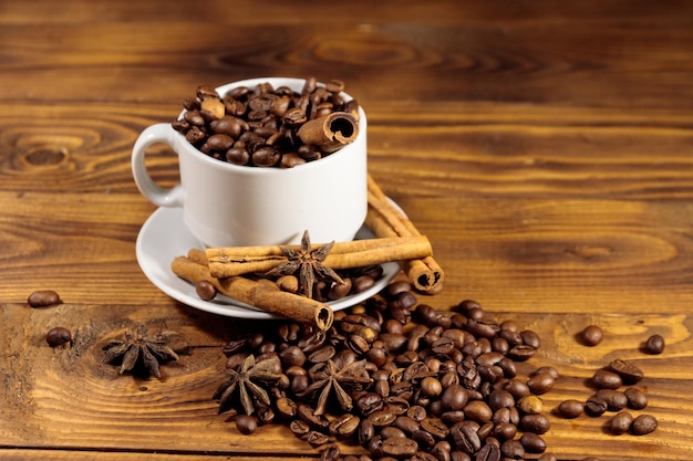 Grãos de café na xícara branca, paus de canela e anis estrelado na mesa de madeira