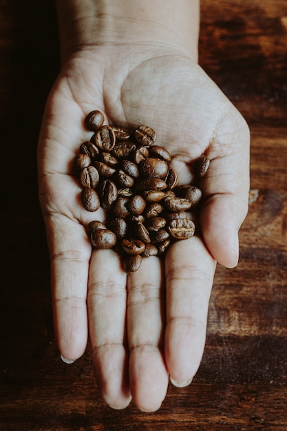 Grãos de café nas mãos do coração em forma de mesa de madeira estilo escuro e vintage