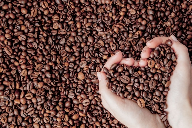 Grãos de café nas palmas das mãos em forma de coração no fundo do café