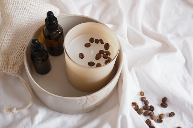 Foto grãos de café, óleo aromático ou soro e vela aromática em um lençol branco, conceito de spa ecológico, bolsa de malha com esponjas de algodão