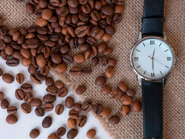 Grãos de café são espalhados em um guardanapo de tela e relógio manual hora do café almoço uma vista de abo
