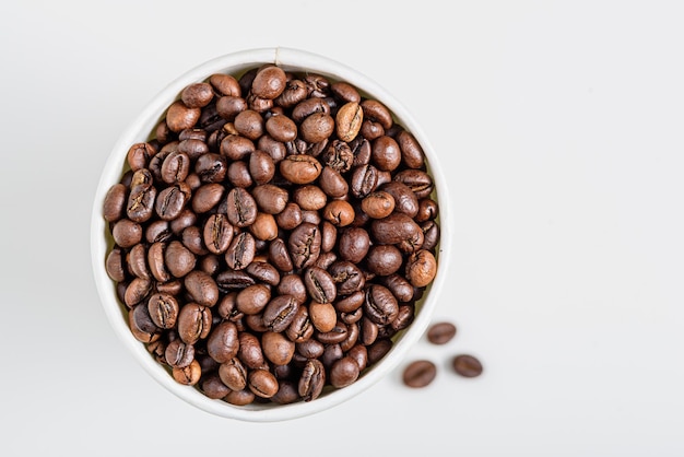 Grãos de café torrados de vista superior em copo branco sobre branco