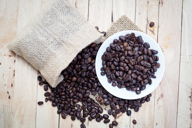 Grãos de café torrados, despejados de um saco na mesa de madeira