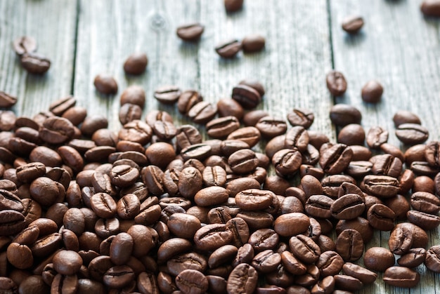 Grãos de café torrados empilhados na parte inferior de uma superfície de madeira rústica cinza, iluminada por trás com luz natural