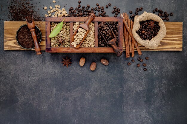 Grãos de café torrados escuros e não torrados, verdes e marrons, em caixa de madeira com conchas instaladas em pedra escura.