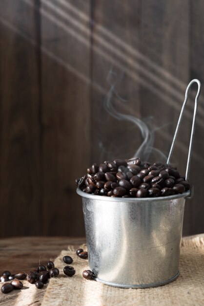 Grãos de café torrados na lata galvanizada sobre a mesa de madeira de grunge