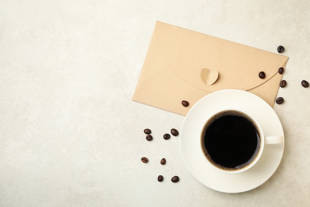 Grãos de café, xícara de café e envelope no plano de fundo texturizado