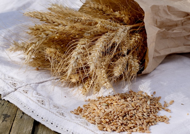 Grãos de trigo sobre toalhas de mesa brancas de linho vintage. Tiro macro de foco seletivo. Ingredientes para o pão, uma velha mesa de madeira. Natureza morta rústica