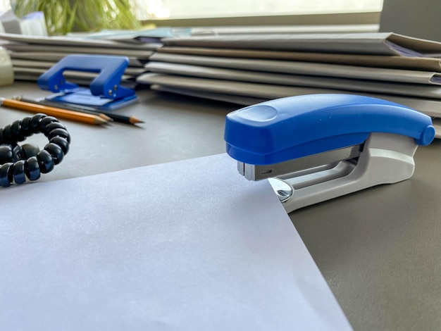 Una grapadora azul grande para grapar papel se encuentra junto a las carpetas de documentos en el trabajo