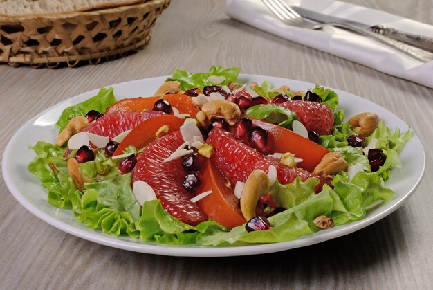 Grapefruit-Kaki-Salat in Salatblättern mit Cashewkernen, Mandeln, Granatapfel