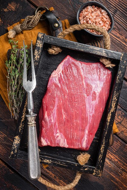 Grasgefüttertes rohes Flankenrindfleischsteak in Holzschale mit Kräutern Holzhintergrund Draufsicht