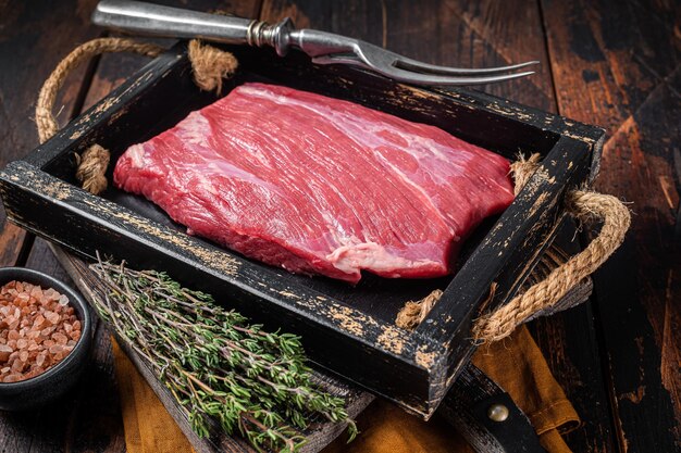 Grasgefüttertes rohes Flankenrindfleischsteak in Holzschale mit Kräutern Holzhintergrund Draufsicht