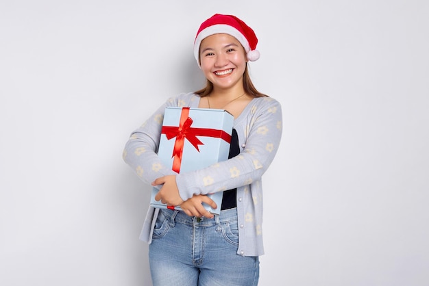 Gratidão e agradecimentos Linda jovem asiática em um chapéu de Papai Noel Carregando uma caixa de presente isolada no fundo branco do estúdio Feliz Natal Conceito