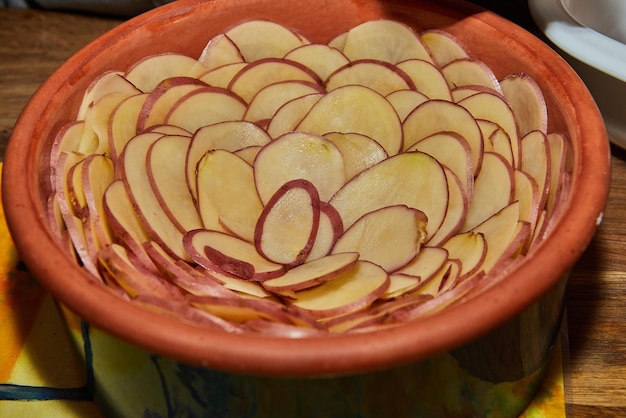 El gratinado de patata en un plato de cerámica con forma de flor está listo para hornearse en el horno