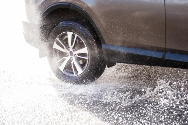 Graue Autokreuzungspfütze mit Wasserspritzern bei Tageslicht, Nahaufnahme mit Defokussierungstechnik