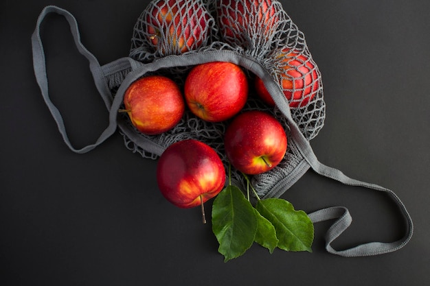 Graue Einkaufstasche aus Mesh mit roten Äpfeln auf schwarzem Hintergrund Kein Konzept für Plastiktüten Ansicht von oben Nahaufnahme