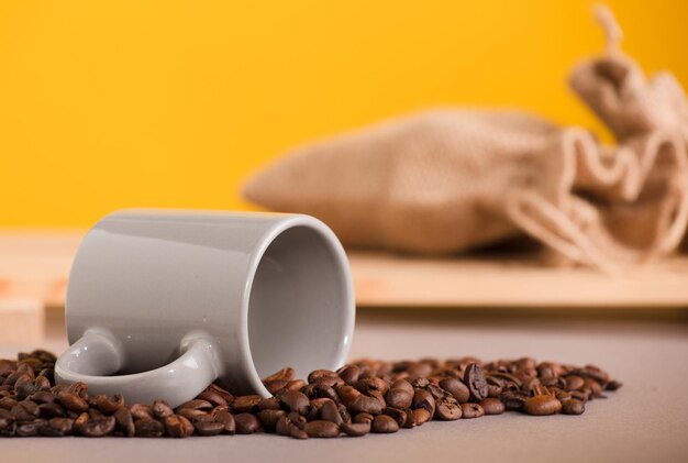 Graue Tasse Kaffee und geröstete Kaffeebohnen-Raphiasäcke mit gelbem Hintergrund