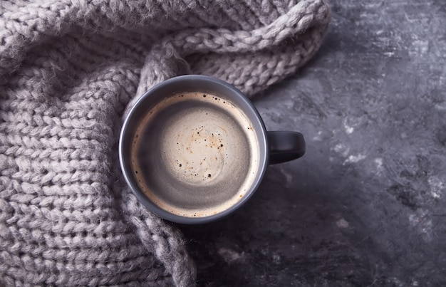 Grauer Becher Kaffee und Schal auf der grauen Tabelle. Herbst-Konzept. Minimalismus.