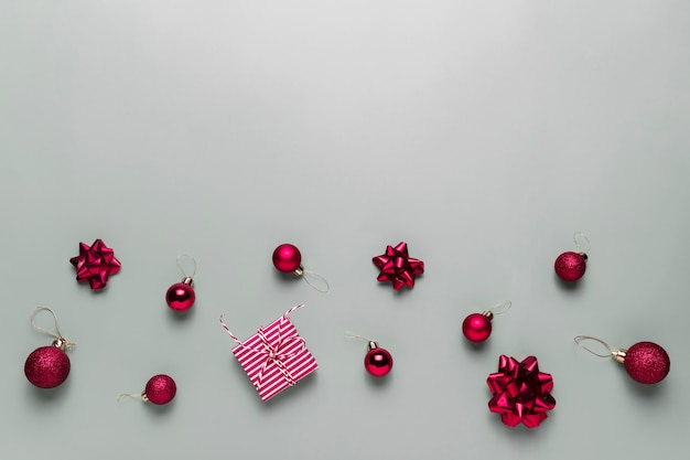 Grauer Hintergrund mit rosa Weihnachtsgeschenkbox vorhanden, kleine rote Weihnachtskugeln oder Kugelspielzeug, Bandschleifen für Tannenbaum, andere Dekorationen. Weihnachtsverkauf, Shopping oder Grußkarte oder Einladung