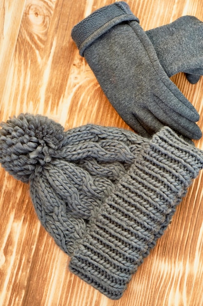 Grauer Hut und Handschuhe auf einer Holzoberfläche gestricktDas Konzept soll im Herbst oder Wintertag warm bleiben