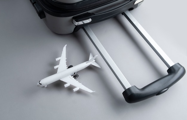 Grauer Koffer der flachen Lage mit Miniflugzeug auf Grau