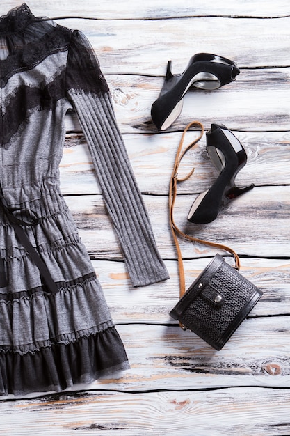 Graues Kleid und schwarze Tasche. Luxus-Heels und klassische Geldbörse. Die dunkle Frühlingskleidung der Dame. Ware zu extrem günstigen Preisen.