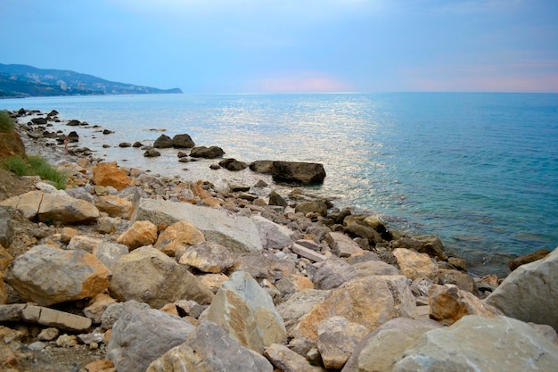 Graues Meer mit Felsen am Strand und rosa Horizont