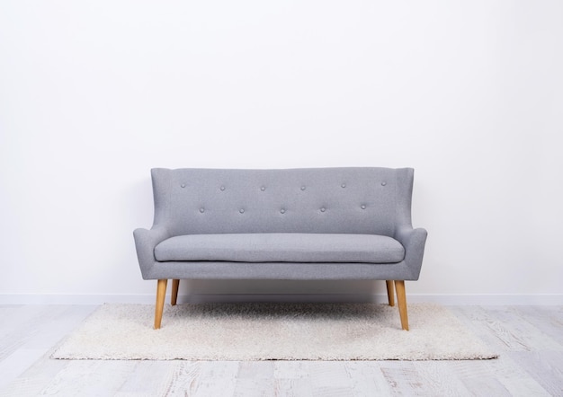 Graues Sofa mit Holzbeinen auf weißem Teppich im hellen Raum installiert