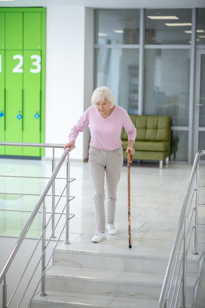 Grauhaarige Frau mit einem Spazierstock geht die Treppe hinunter